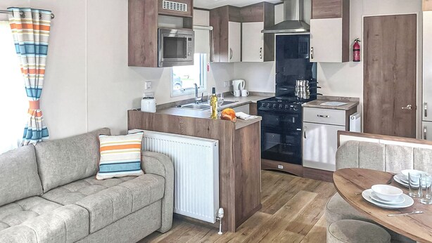 Una cocina compacta con una isla central, un comedor con mesa de madera, un sofá con cojines a rayas y un radiador.