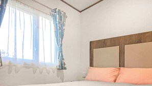 Una cama con cabecera, una ventana con cortinas y una pared con paneles de madera.