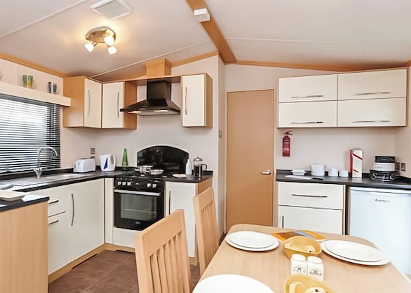 A compact kitchen with a stove, oven, and sink, a dining table with plates, and a fire extinguisher.