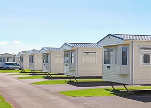 A row of mobile homes with a paved walkway and green grass in front.