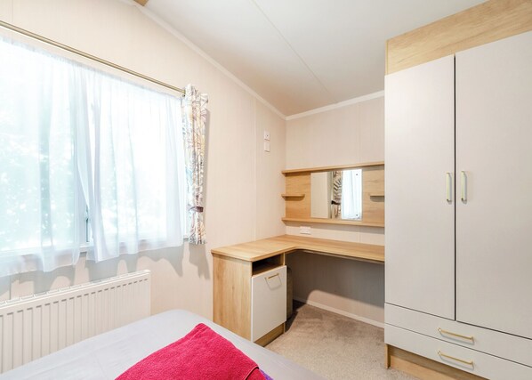 A bedroom with a bed, a desk, a wardrobe, and a window with curtains.