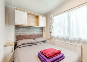 Un dormitorio con cama, cabecera, ventana con cortinas y radiador.