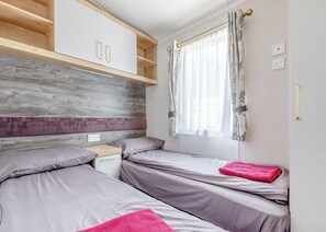 A bedroom with two beds, wooden shelves, a window with curtains, and a nightstand.
