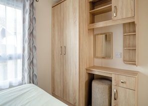 Quarto com cama, guarda-roupa de madeira, espelho e prateleiras embutidas.