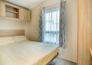 Un dormitorio con cama, cabecero de madera, ventana con cortinas estampadas y armario de madera.