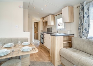 A compact kitchenette with a stove, oven, and sink. There is a dining area with a table set for two, and a sofa.