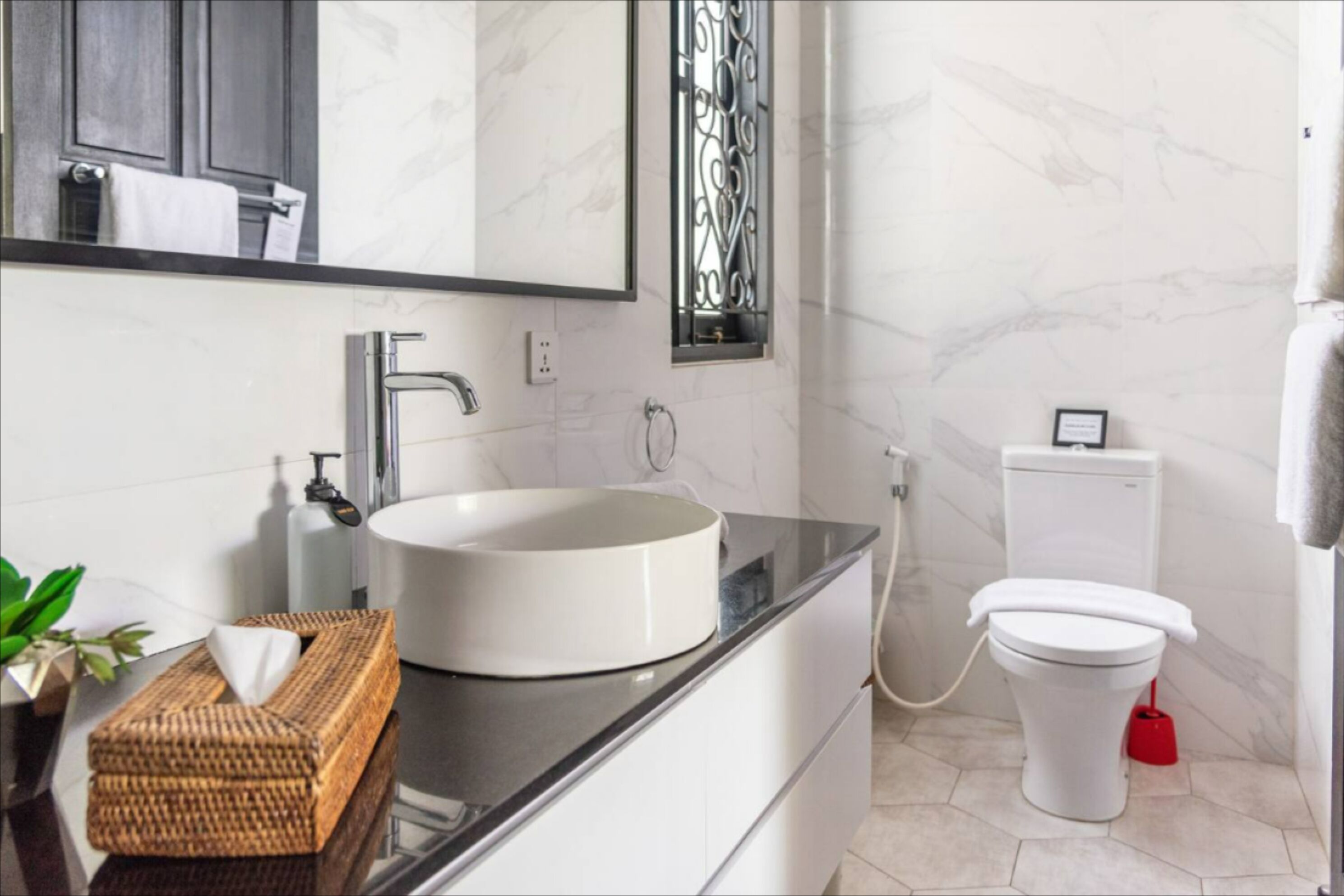 A modern bathroom with a white sink, a mirror, a toilet, and a red bidet.