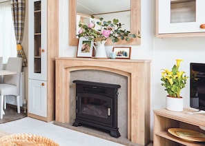 Een woonkamer met een open haard, een spiegel, een vaas met bloemen en een televisie.