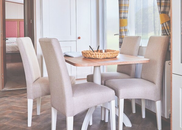 A dining area with a round table, four chairs, and a woven basket on the table. - Spacious and luxurious 12-foot-wide caravan with one double and one twin. (Axminster)