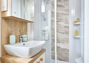 Een badkamer met een wit wastafelmeubel, een douche en een spiegel boven het wastafelmeubel.