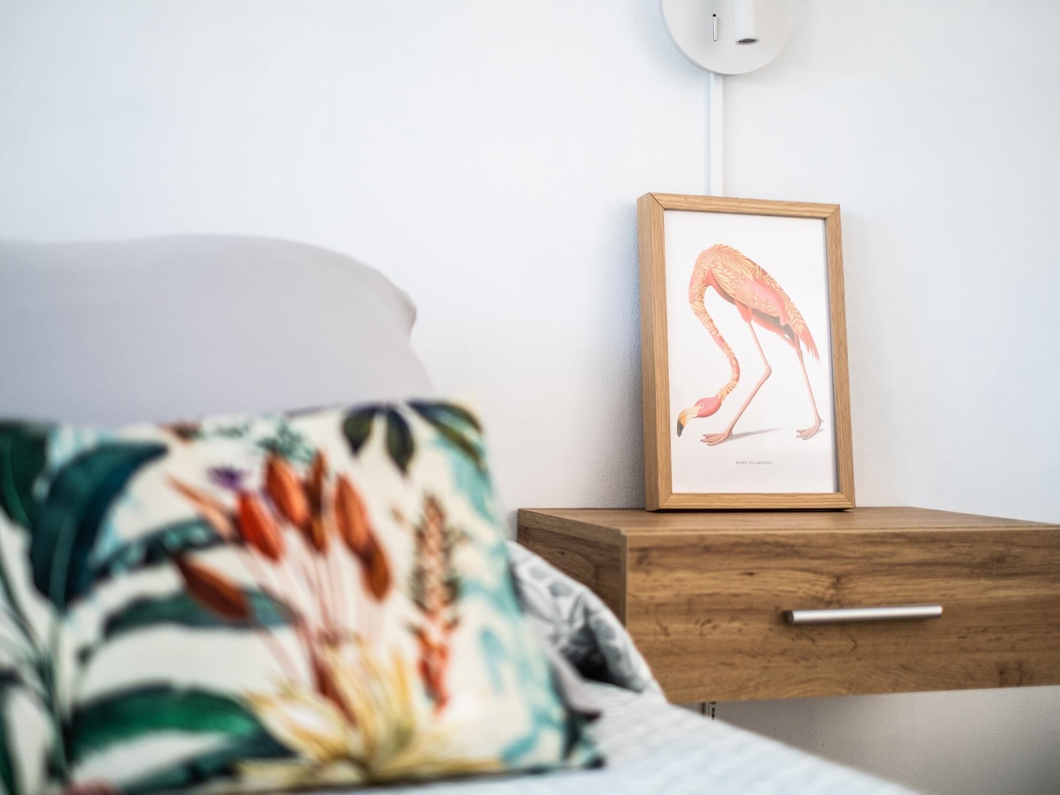 Una camera da letto con un letto, un comodino e un'opera d'arte incorniciata raffigurante un fenicottero.