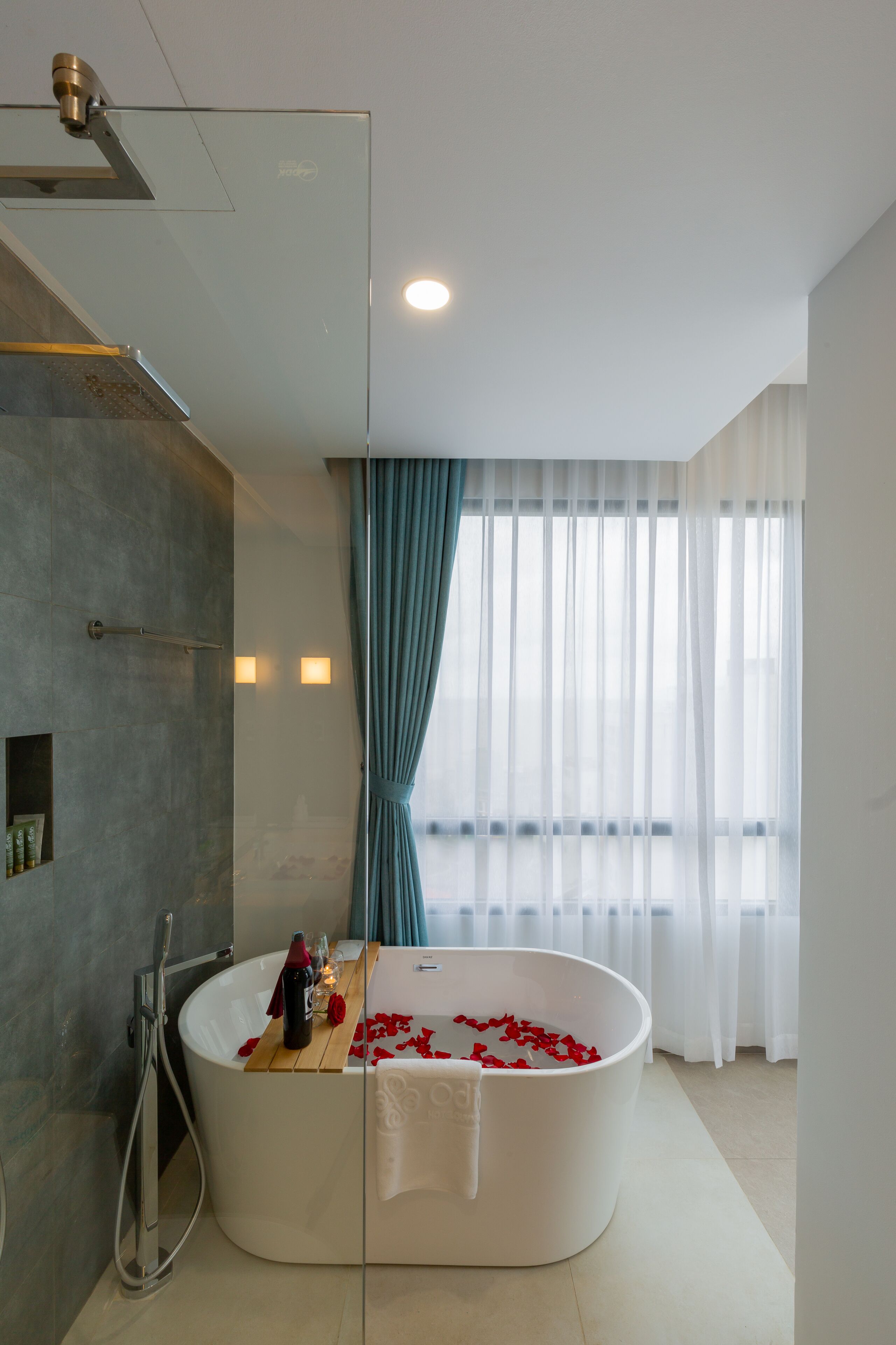 A modern bathroom with a freestanding bathtub, a glass shower enclosure, and a view of the outdoors through sheer curtains.