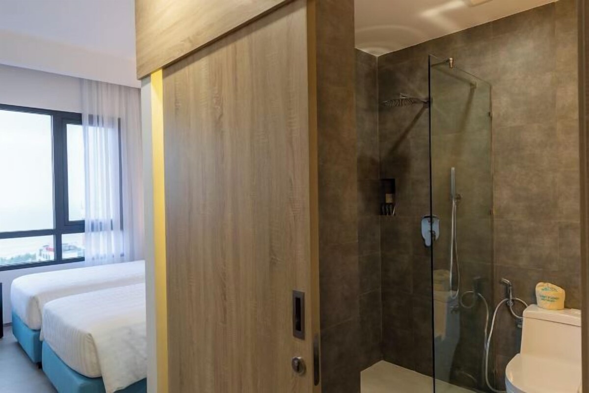 A hotel room with a large window, a shower with glass doors, and two beds.