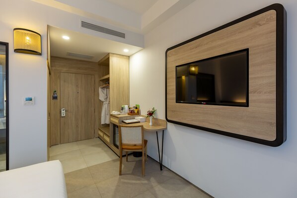 Habitación de hotel con puerta de madera, una mesita pequeña con una silla, un televisor montado en la pared y una lámpara fijada a la pared.