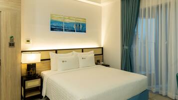 Habitación de hotel moderna con una cama grande, una mesita de noche, una lámpara de pared y vistas al exterior a través de cortinas translúcidas.