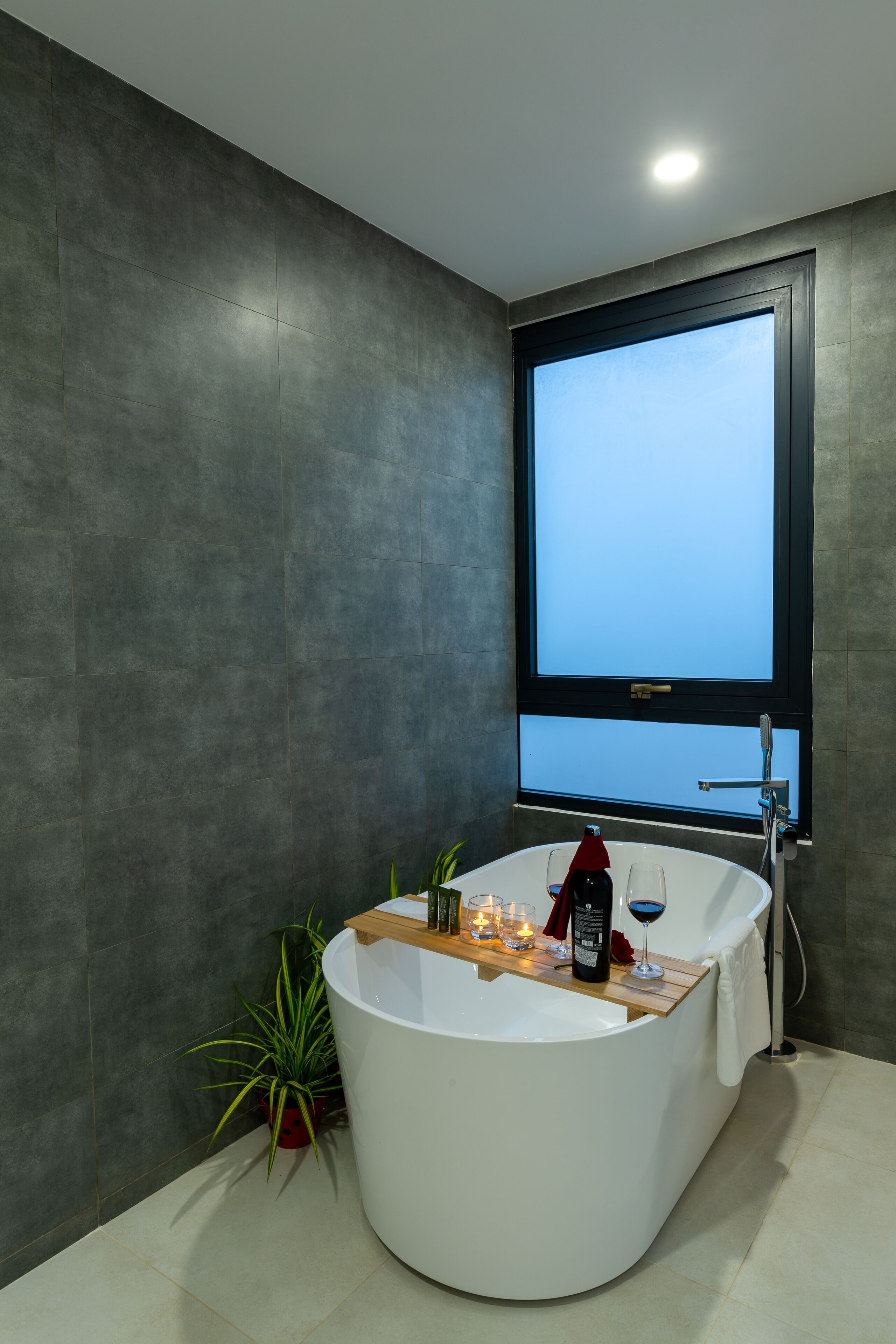 A modern bathroom with a freestanding bathtub, a window, and a potted plant.