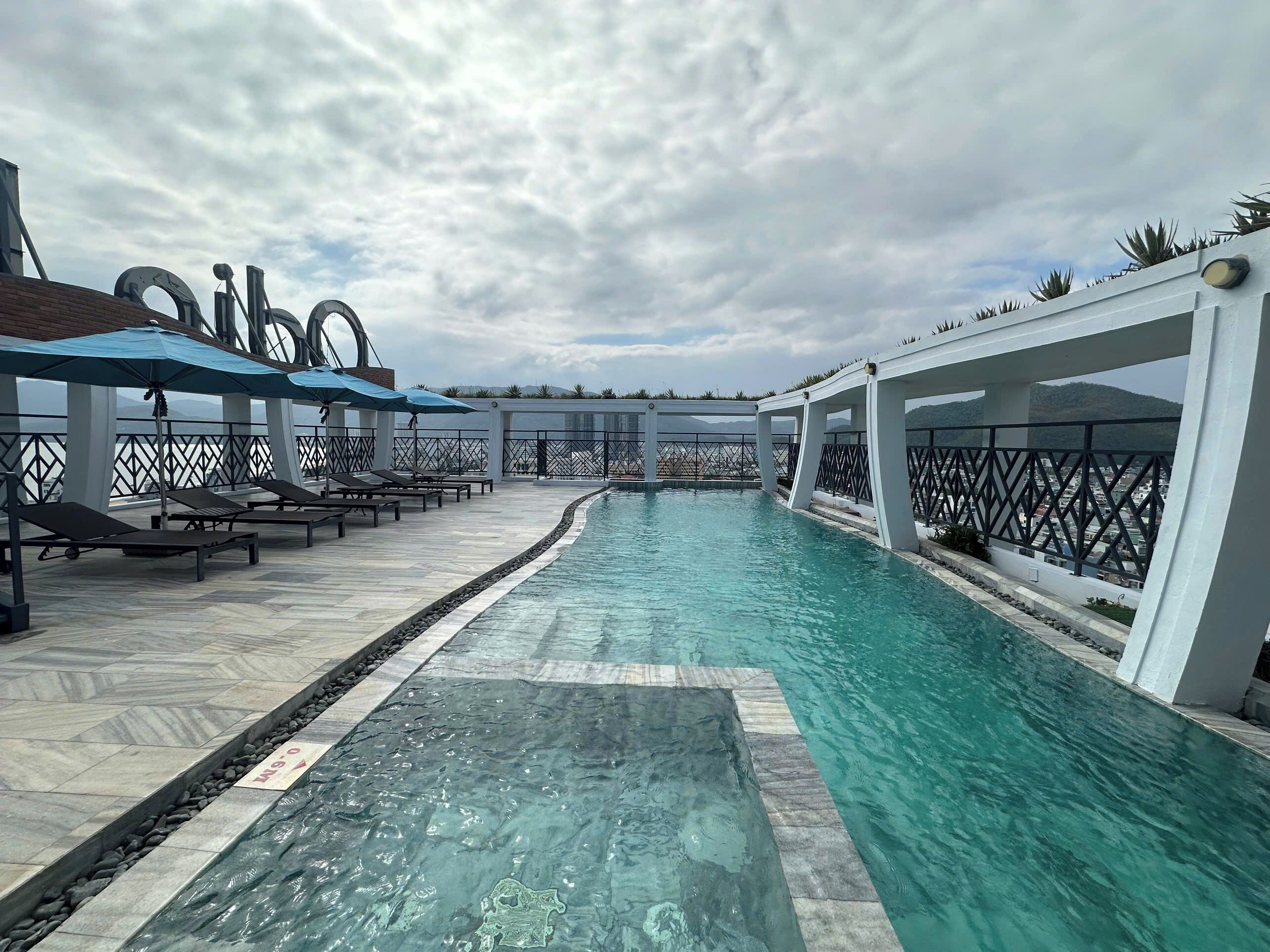 A swimming pool with lounge chairs and umbrellas, surrounded by a white fence and a view of the mountains.