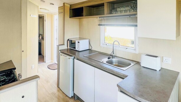 Una kitchenette compacta con microondas, lavamanos y tostadora, que cuenta con una ventana sobre el lavamanos.