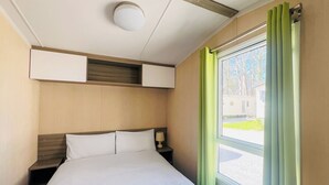 Habitación de hotel con cama, mesita de noche, lámpara, luz de techo y ventana con cortinas.