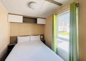 Een hotelkamer met een bed, nachtkastje, lamp, plafondlamp en een raam met gordijnen.