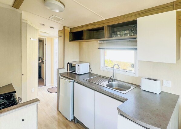 A compact kitchenette with a microwave, sink, and toaster, featuring a window above the sink.