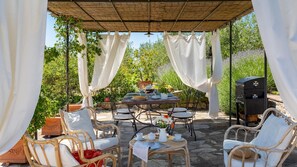 An outdoor patio with a table set for dining, surrounded by wicker chairs and a barbecue grill.