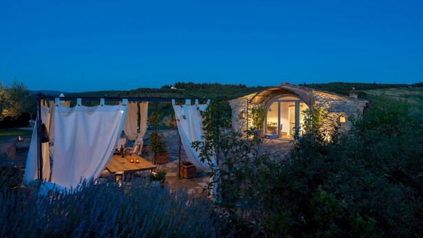 A stone house with a large arched doorway, a covered outdoor seating area with white curtains, and a view of the surrounding landscape. - Country House Lo Spigo 4 (Barberino Tavarnelle)