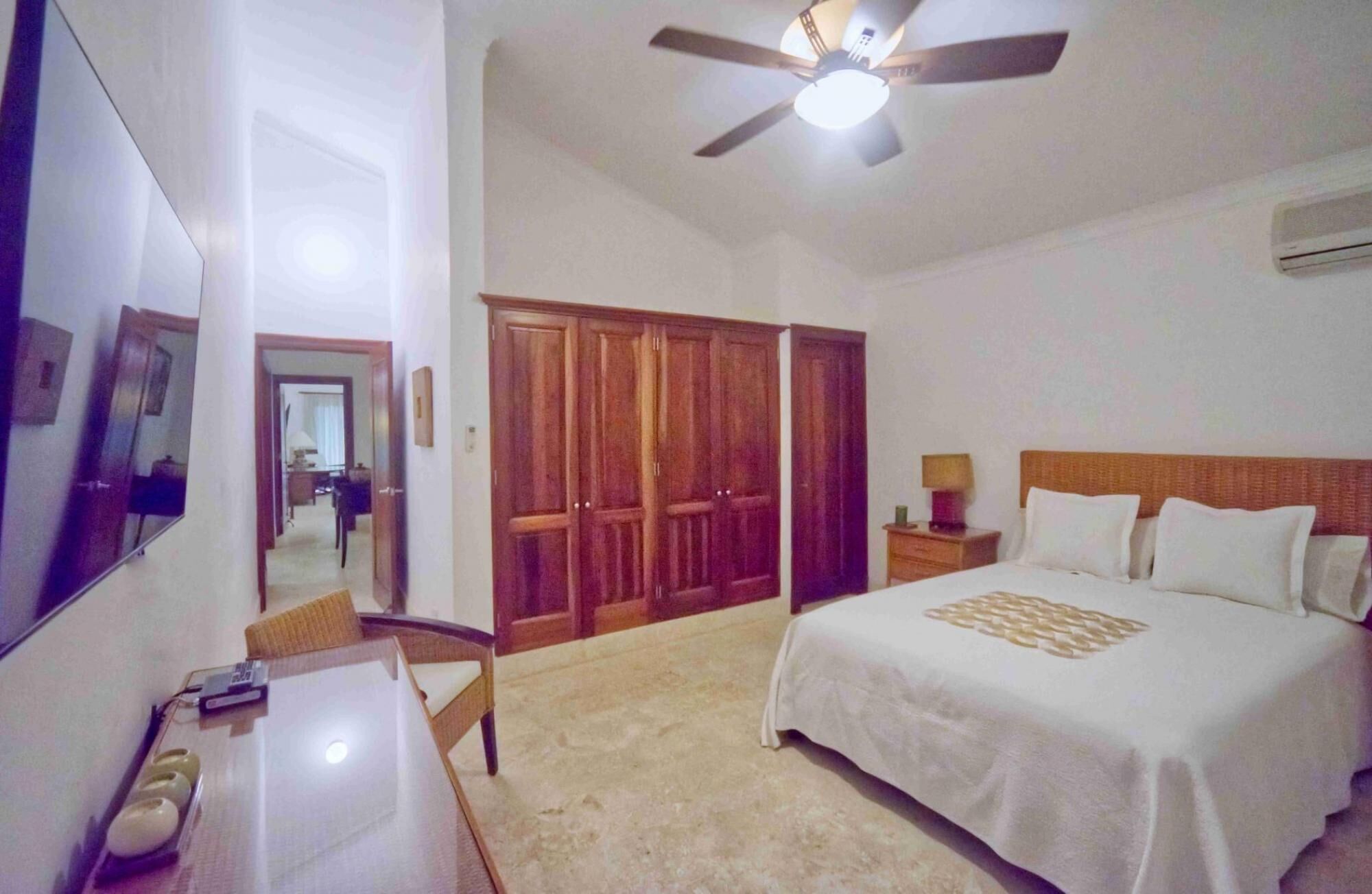 A hotel room with a bed, a desk, a chair, a wardrobe, and a ceiling fan.