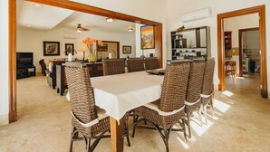 Un coin repas avec une longue table et des chaises en osier, une nappe blanche et un vase rempli de fleurs.