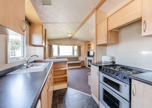 A compact kitchen with a sink, stove, and oven, wooden cabinets, and a window providing natural light.