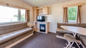 A compact RV interior with a sofa, a TV, a fireplace, and a dining area. - 12ft-wide caravan with one double and two twin. (Bognor Regis)