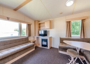 Interior compacto de autocaravana con sofá, televisión, chimenea y comedor.
