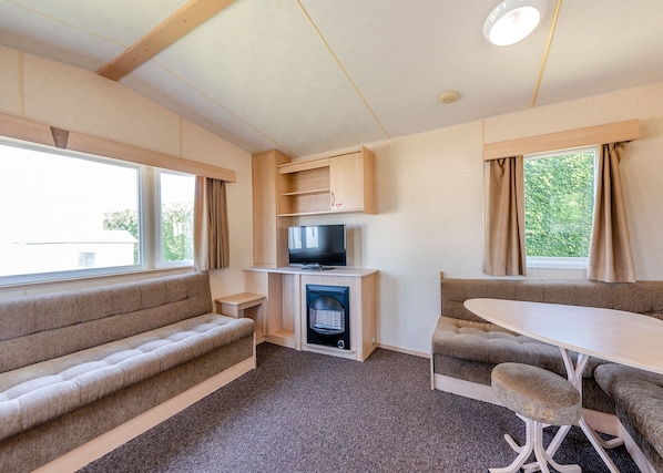A compact RV interior with a sofa, a TV, a fireplace, and a dining area. - 12ft-wide caravan with one double and two twin. (Bognor Regis)