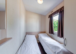 A small, single-room hotel room with two single beds, a window with curtains, and a light fixture.