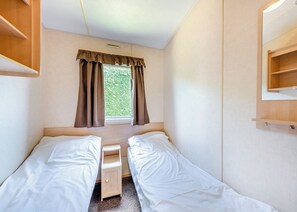 A small, single-room accommodation with a bed, a window, and a wooden shelf. - 12ft-wide caravan with one double and two twin. (Bognor Regis)