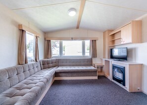 A cozy RV interior with a sectional sofa, a flat-screen TV, and a fireplace. - 12ft-wide caravan with one double and two twin. (Bognor Regis)