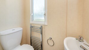 A bathroom with a toilet, a window, a towel rack, and a sink. - 12ft-wide caravan with one double and two twin. (Bognor Regis)