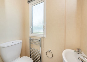 A bathroom with a toilet, a window, a towel rack, and a sink. - 12ft-wide caravan with one double and two twin. (Bognor Regis)