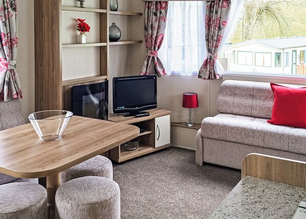 A cozy room with a wooden table, a sofa, a TV, and a lamp.
