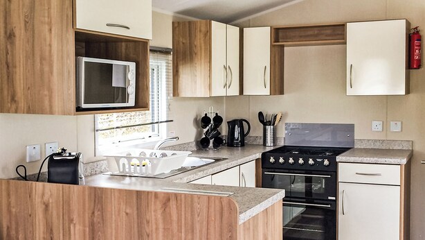 A compact kitchen with wooden cabinets, a microwave, a stove, and a sink. - 3 bedroom accommodation in Buxton (Buxton)