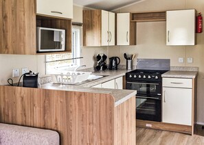 A compact kitchen with wooden cabinets, a microwave, a stove, and a sink.