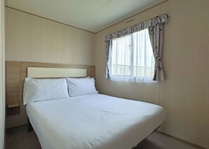 Ein Hotelzimmer mit einem großen Bett, einem Kopfteil, einem Fenster mit Vorhängen und Blick auf Gebäude.