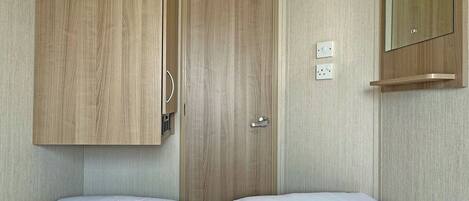 Une chambre avec deux lits simples, une armoire en bois, une porte et un miroir au mur.