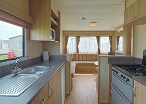 A compact RV kitchen with a sink, stove, and a small dining area. - Caravan with one double and one twin. (Chapel St Leonards, Skegness)