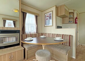 Ein kompaktes Wohnmobil-Interieur mit Esstisch, Sitzbank, Küchenzeile und kleinem Fenster.