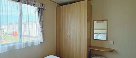 A bedroom with a bed, a wardrobe, a small stool, a mirror, and a window with curtains.
