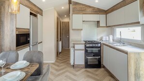A modern kitchen with a built-in oven, a microwave, and a dining area with a table set for two. - 12ft-wide luxury caravan with one double and two twin. (Charmouth)