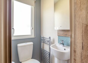 Ein kleines Badezimmer mit Toilette, Fenster, Waschbecken und Handtuchhalter.