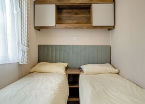 A small, compact room with two single beds, a wooden headboard, and a built-in shelf above the beds.