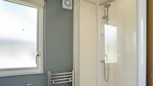 A bathroom with a shower, a toilet, a towel rack, and a window. - 12ft-wide luxury caravan with one double and two twin. (Charmouth)